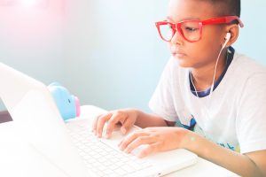 Little boy child wearing red glasses listening and using laptop computer