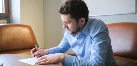 Man writing on a piece of paper while sitting at his desk