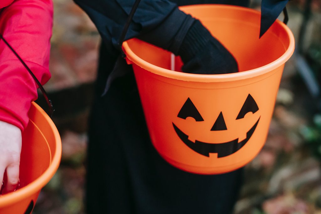 Cropped photo of kids holding treats in an orange jack-o-lantern bucket