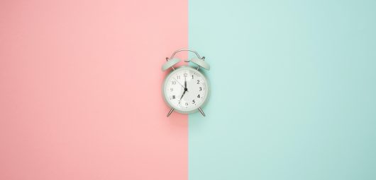 Gray double bell clock on top of split pink and blue background