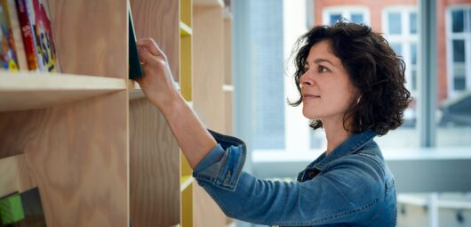 Woman in denim jacket browsing a shelf of library books