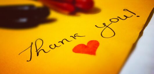 The words thank you written on a yellow paper with a red heart colored in